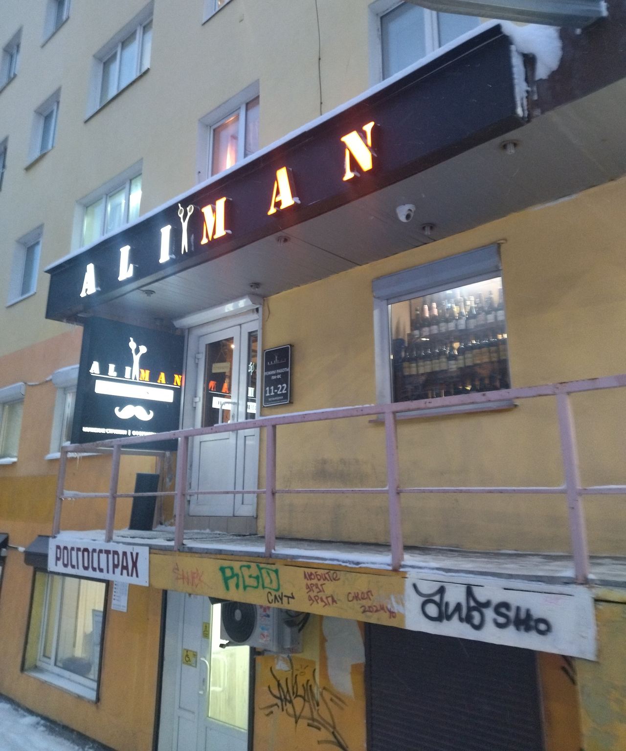 Вход в студию зимой: лестница с перилами, над дверью светящаяся вывеска ALIMAN